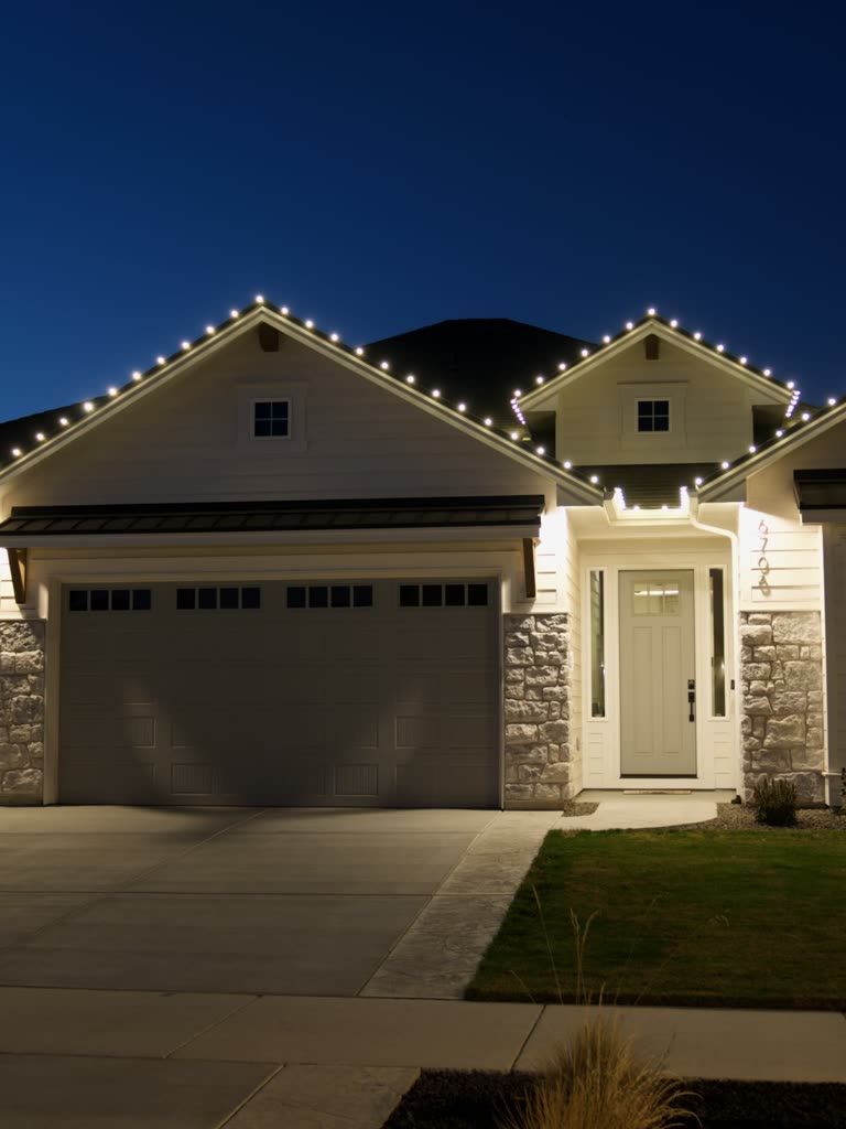 A Boise home at twilight with warm white lights along every roofline